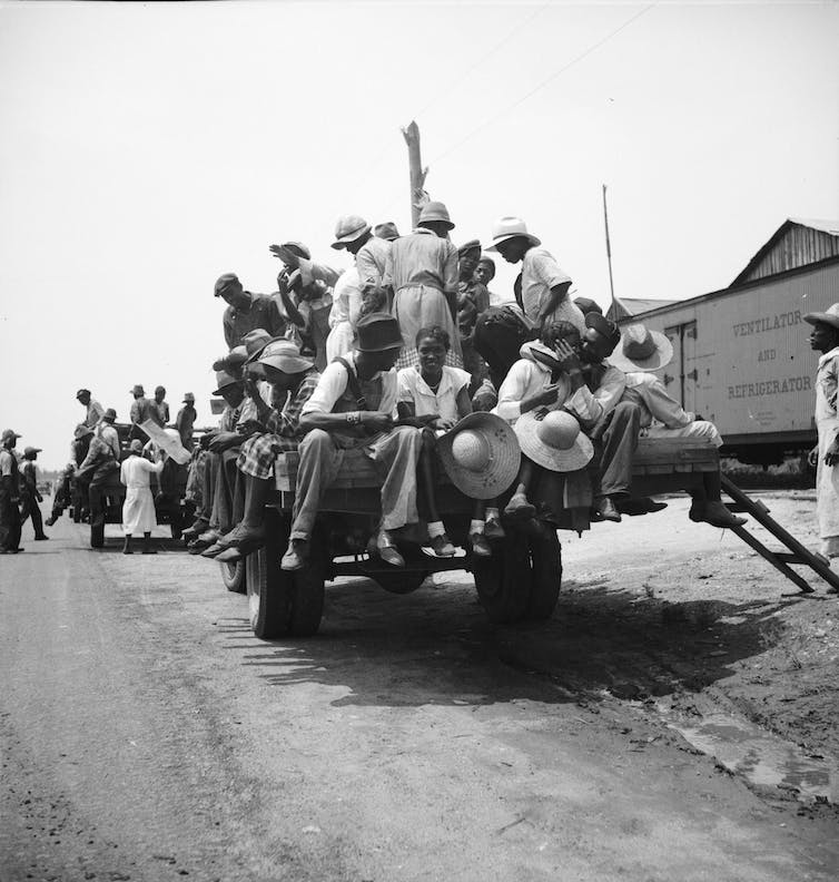 African American men and women sitting and standing on the back of a truck.
